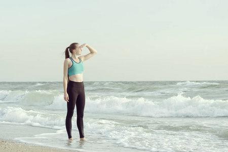 女孩在沙滩上穿运动服看着远方。晨阳