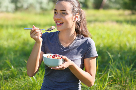 美丽的年轻妇女吃可口的燕麦片户外