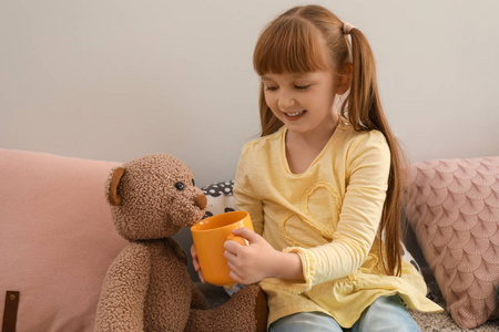 可爱的小女孩在家处理玩具熊与杯子热的可可饮料