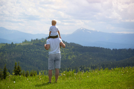 阳光信托父亲带着一个小儿子在他的肩膀上.山上的背景.