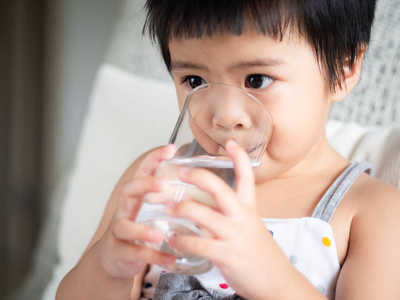 快乐的小可爱女孩拿着杯子喝着水。儿童饮用健康概念