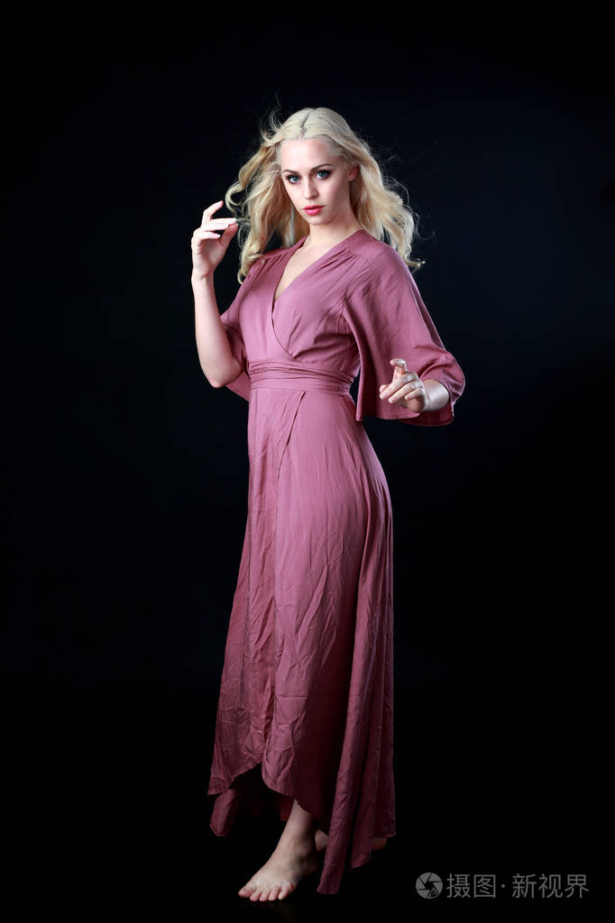 穿着长紫色连衣裙的金发女郎的全长肖像.站立姿势.黑色工作室背景