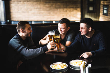男性朋友满足在酒吧里喝着啤酒，吃薯片。欢呼和英国酒馆里玩得开心
