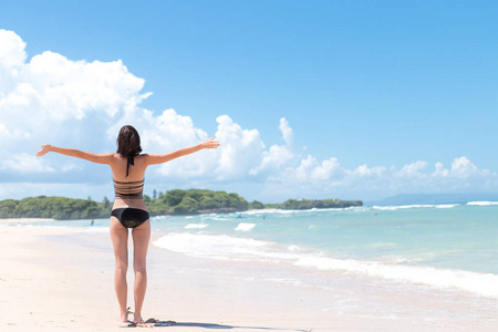 海滩度假。幸福的女人在海滩上享受阳光明媚的日子。张开双臂 自由 快乐和幸福。热带的概念，巴厘岛