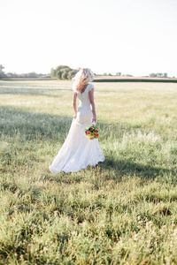 一个美丽的新娘在阳光下的肖像。穿着婚纱的年轻快乐女人正在田野里散步。束。花。夏天。舒适