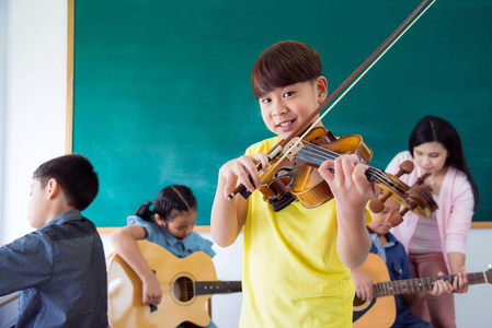 年轻亚洲男孩在学校音乐课上拉小提琴时微笑