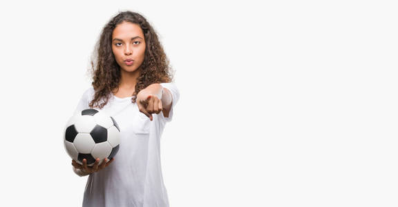 年轻的西班牙裔女子拿着足球球指向相机和你, 手势, 正面和自信的手势从前面