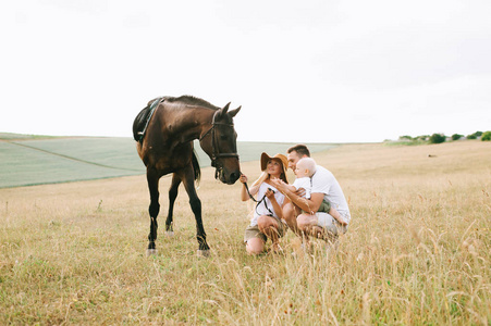 年轻的家人在田野里玩得很开心。父母和孩子与马在领域