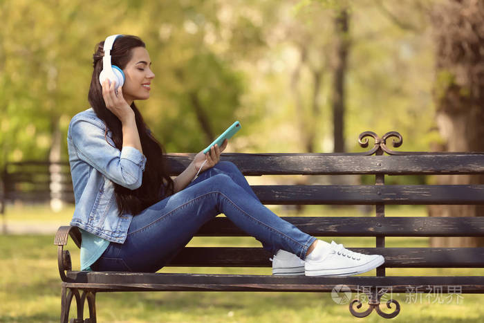 在公园休息的美丽的年轻妇女听音乐