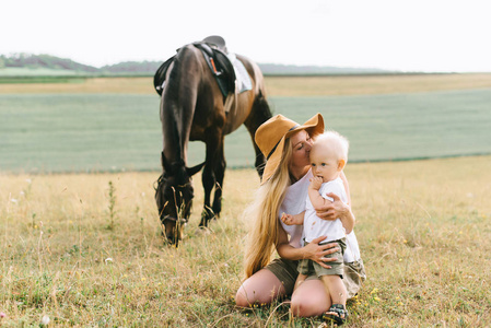 年轻的女人和小男孩在田里玩得很开心。在田野里有一匹马的父母和孩子
