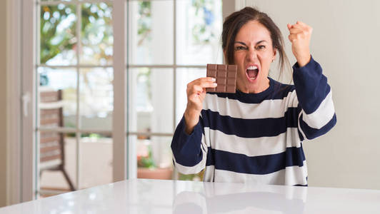 中年妇女吃巧克力酒吧懊恼和沮丧的呼喊与愤怒, 疯狂和叫喊与举手, 愤怒的概念