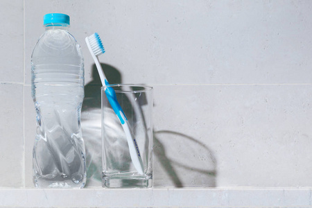 清洁白色牙刷与蓝色修剪在明确的饮水玻璃和一瓶饮用水在货架上复制空间, 良好的健康牙齿和牙齿或清洁生活方式的概念