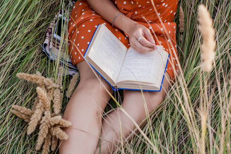 美丽快乐的金发女郎在小穗和小麦领域的书上日落, 在草地上