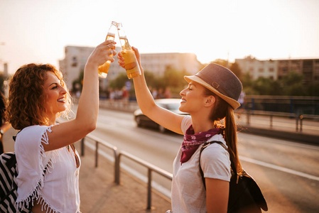 夏天, 两个漂亮的时髦女人在城市街道上敬酒。