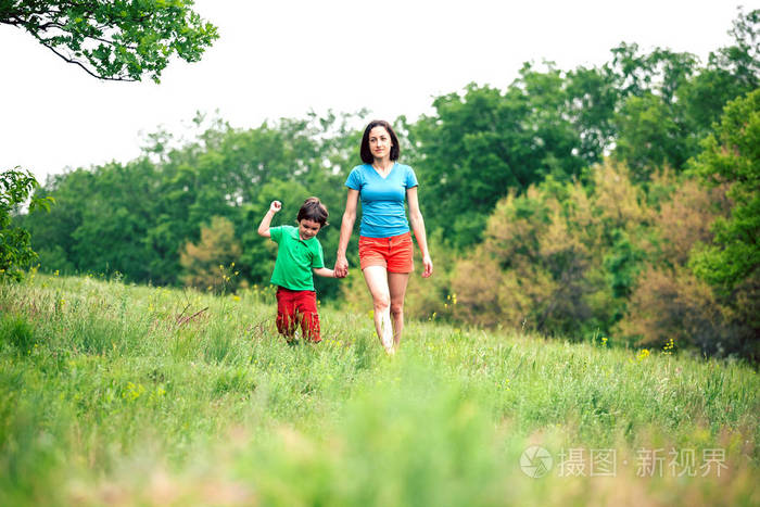 男孩和他的母亲在草地上散步。一个女人牵着她儿子的手。孩子和妈妈正沿着田野走。绿草