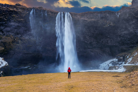 Seljalandsfoss 瀑布在冰岛。穿红夹克的家伙看 Seljalandsfoss 瀑布