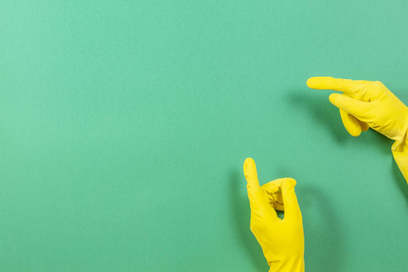 妇女手用黄色橡胶手套点向上与手指, 在绿色背景之下