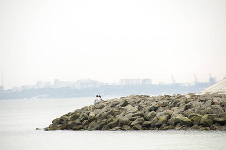 海边的恋人坐在岩石上看着城市