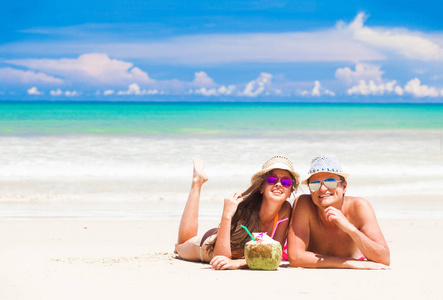 年轻夫妇放松在热带海滩与新鲜的椰子鸡尾酒