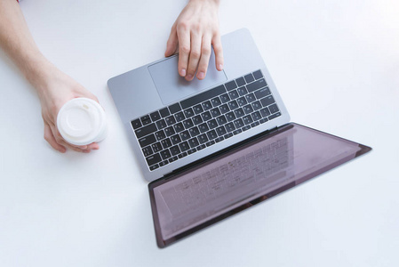 在一台笔记本电脑上工作, 在白色的背景下拿着一杯咖啡