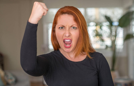 红发的女人在家里恼怒和沮丧的呼喊与愤怒, 疯狂和叫喊与举手, 愤怒的概念