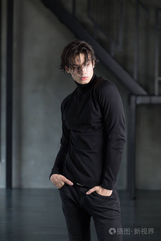 时尚英俊的年轻男子与湿深色的头发在所有黑色的衣服与高领毛衣和撕裂