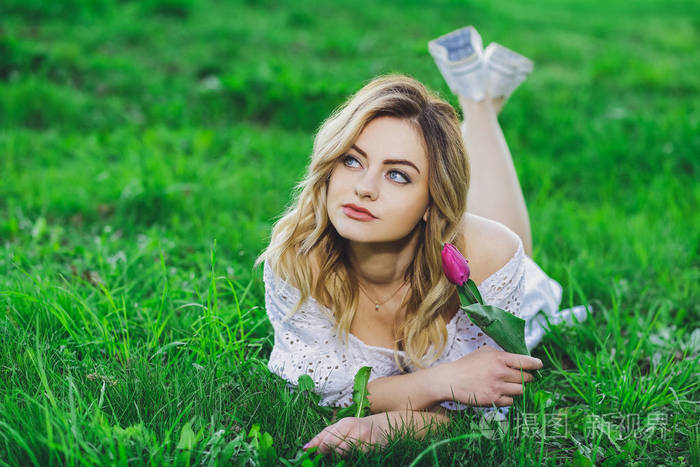 年轻美丽的金发女孩在白色礼服与花郁金香在背景绿色草