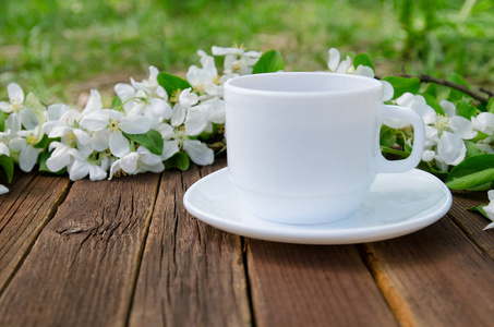 上一张小木桌，苹果树上的花在背景上的白色杯子。侧视图