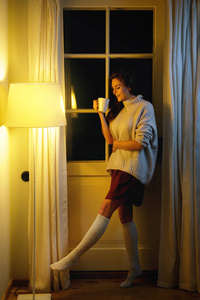 穿着保暖毛衣和袜子的漂亮女人正在喝热茶或咖啡。
