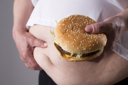妇女在手患肥胖与大的汉堡包。垃圾食品的概念