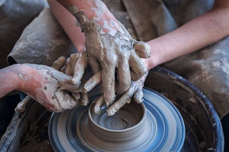 女人和男人的手。波特在工作。创建的菜肴。窑匠。脏手在粘土和匠心之轮轮与产品