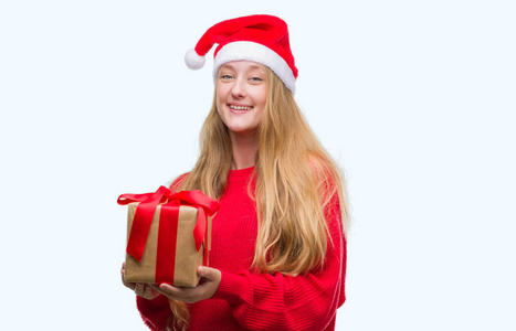 穿着圣诞老人帽子的金发女郎带着一张笑脸站着, 微笑着露出一副自信的笑容。