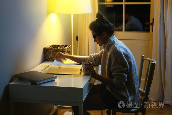 穿一件保暖羊毛衫的女人正在半夜看书.