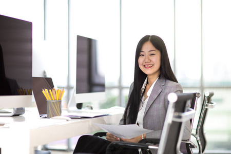 美丽的亚洲商务妇女坐在椅子上, 微笑着在现代办公室与新的台式计算机