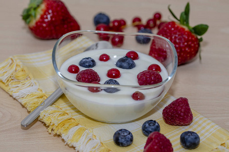 树莓, 蓝莓, 草莓和黑莓酸奶在一个木桌上的黄色餐巾上的玻璃碗
