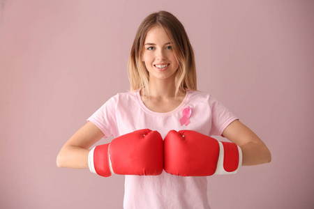 美丽的女人与粉红色丝带和拳击手套的颜色背景。乳癌概念