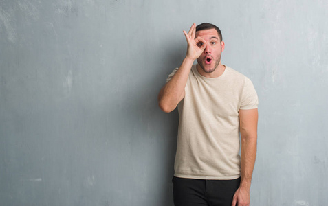 年轻的白种人在灰色的垃圾墙做 ok 手势震惊与惊讶的脸, 眼睛看着通过