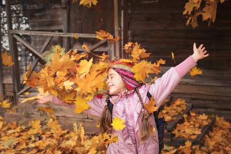 女孩扔枫叶.秋天的乐趣.学校放假.在树叶秋天玩耍的孩子照片