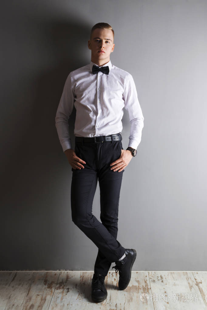 英俊的年轻男子在白色衬衫和弓领带摆在灰色演播室, 全身照片-正版