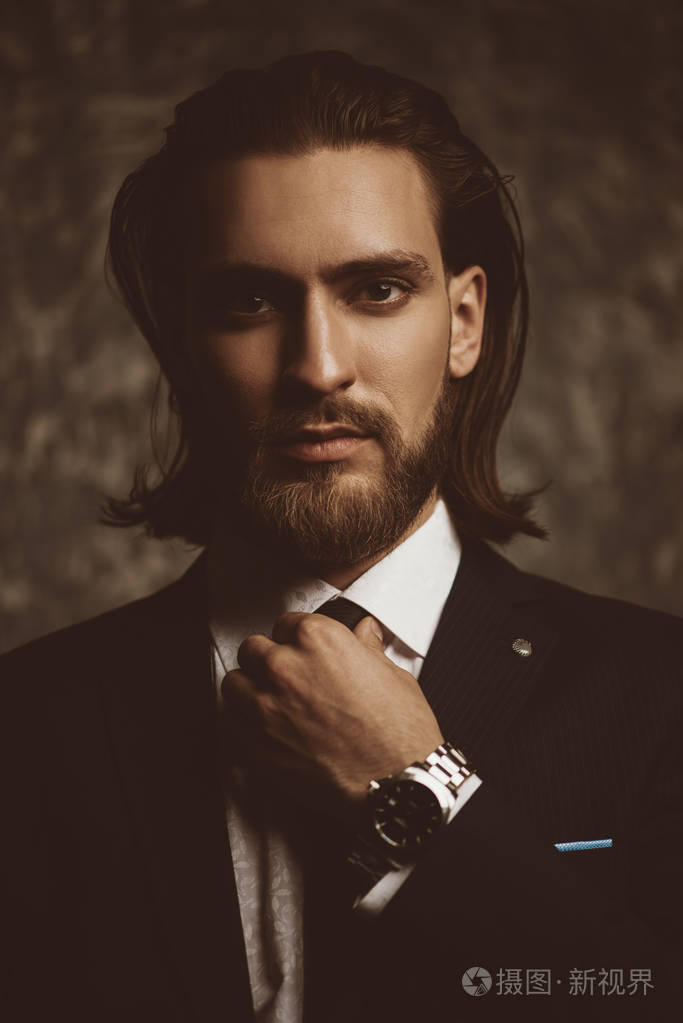 时尚镜头英俊的年轻人穿着优雅的西装和白色衬衫的黑暗背景.