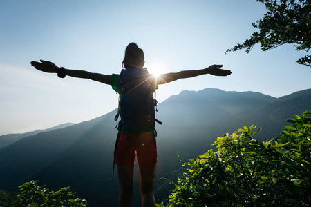 成功的女性徒步旅行者与 outstreched 胳膊站立在山顶在日出期间