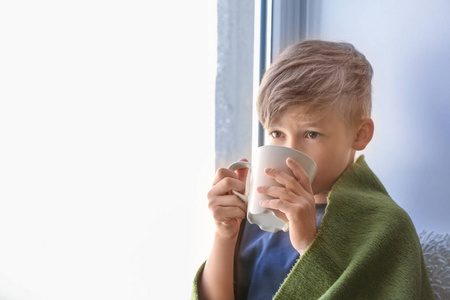 可爱的小男孩与杯子热可可饮料在窗口附近