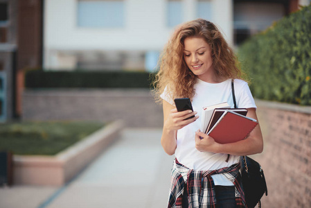 女学生在校园漫步时使用智能手机和手持书本