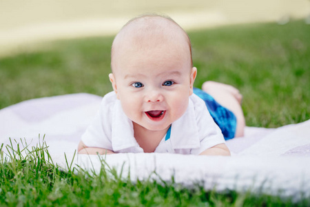 特写肖像的可爱滑稽白种白人男孩与蓝灰色的眼睛躺在草地上公园。认识可爱的婴儿在白色背景户外