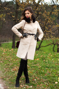 与秋天的公园里走一袋米色外套年轻美丽的女人的画像