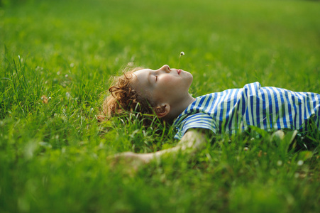 这个8岁的男孩躺在茂密的绿草中的背上。