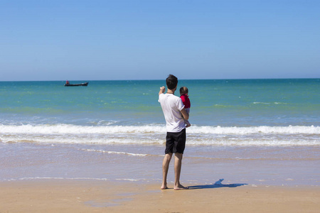 年轻的爸爸带着小女儿看海浪, 快乐的家庭放松