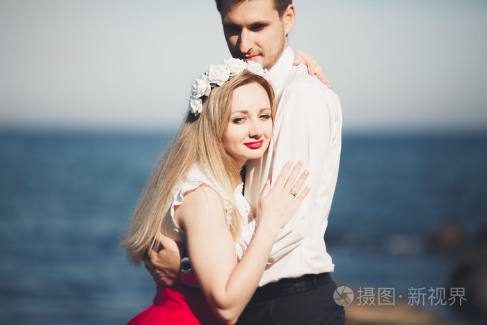 浪漫恩爱的夫妻,靠近海,蓝色天空的石头上摆姿势
