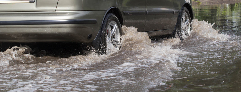 在后场大雨造成洪水期间被水淹没的道路上行驶的汽车