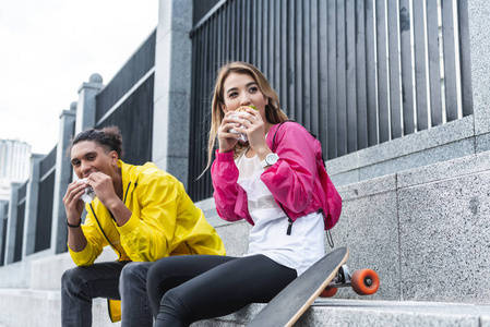城市街滑板附近多文化情侣吃汉堡包的选择性聚焦